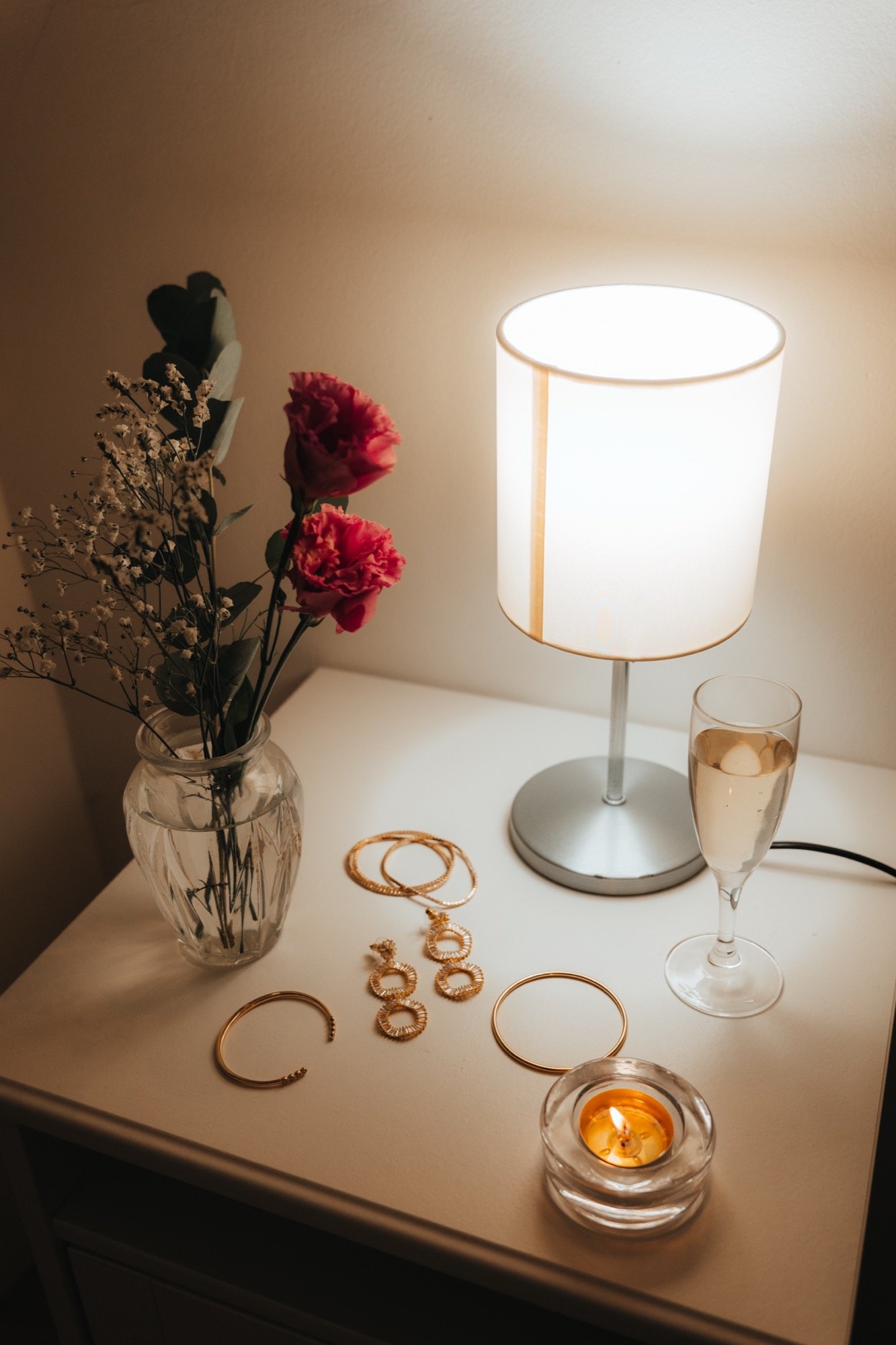 Bijoux, lampe allumée et roses rouges sur une table de nuit