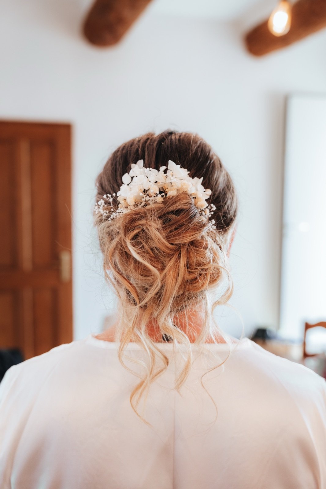 Le chignon fleuri de la mariée, vu de dos, pendant les préparatifs
